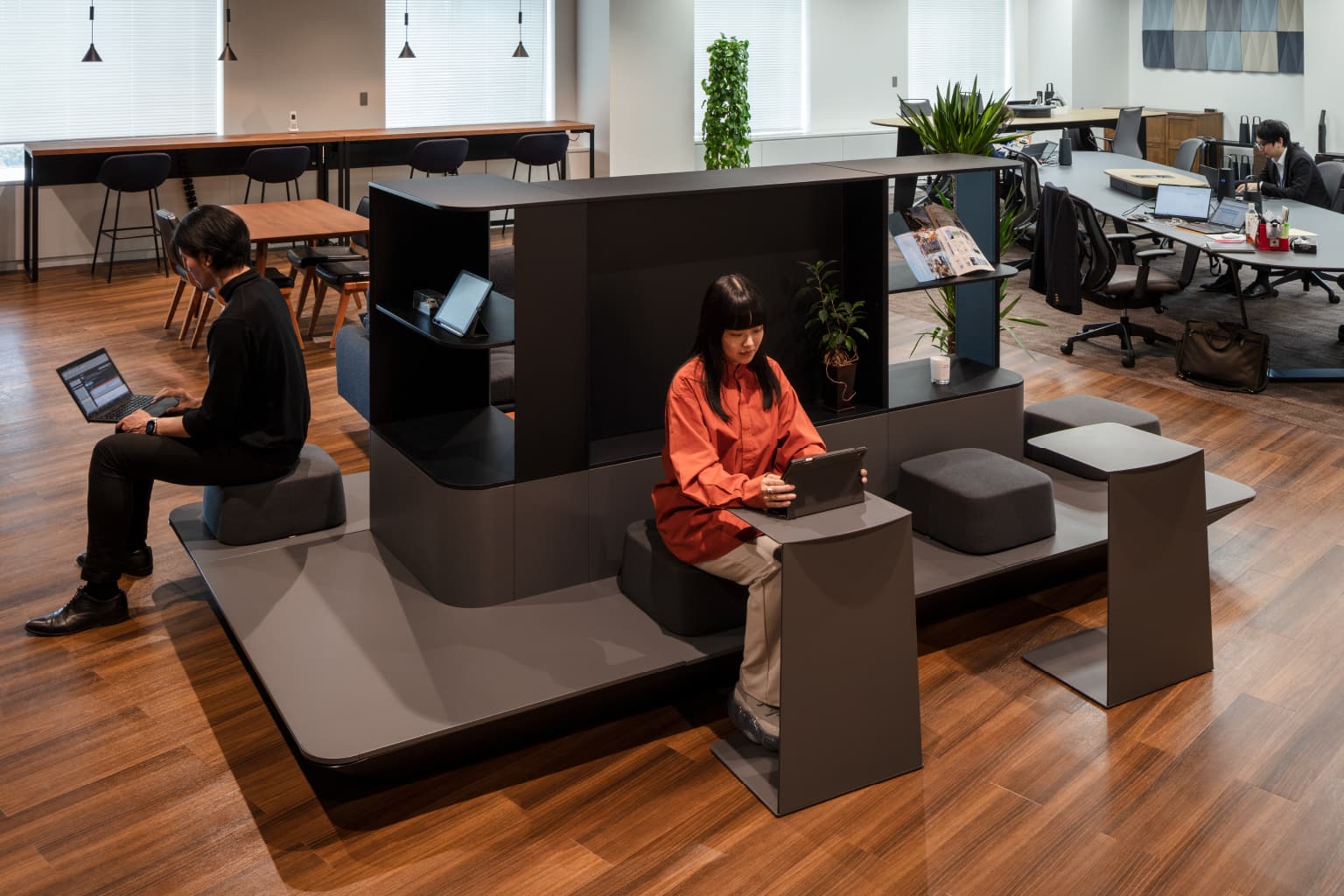 北電情報システムサービス株式会社 様の事例写真／[コミュニケーションエリア]ミニテーブルが置かれた縁側のようなスペースでは、前を通る人との偶発的なコミュニケーションが生まれ、自然と人が集まる場になっています。奥にある執務エリアや休憩スペースの目隠しの役割も。壁を建てずに空間をゆるやかに区切っています。