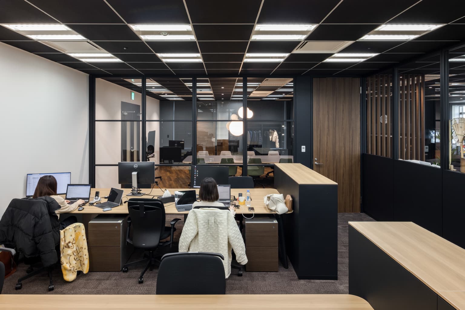 北電情報システムサービス株式会社 様の事例写真／[執務エリア（開発部）]開発部は機密情報を取り扱うため、グループアドレスを採用した個室の執務スペースで業務に当たっています。壁の２面にガラスを使うことで閉塞感を軽減しつつも、黒い格子で視線をゆるやかに遮っているのが特徴です。