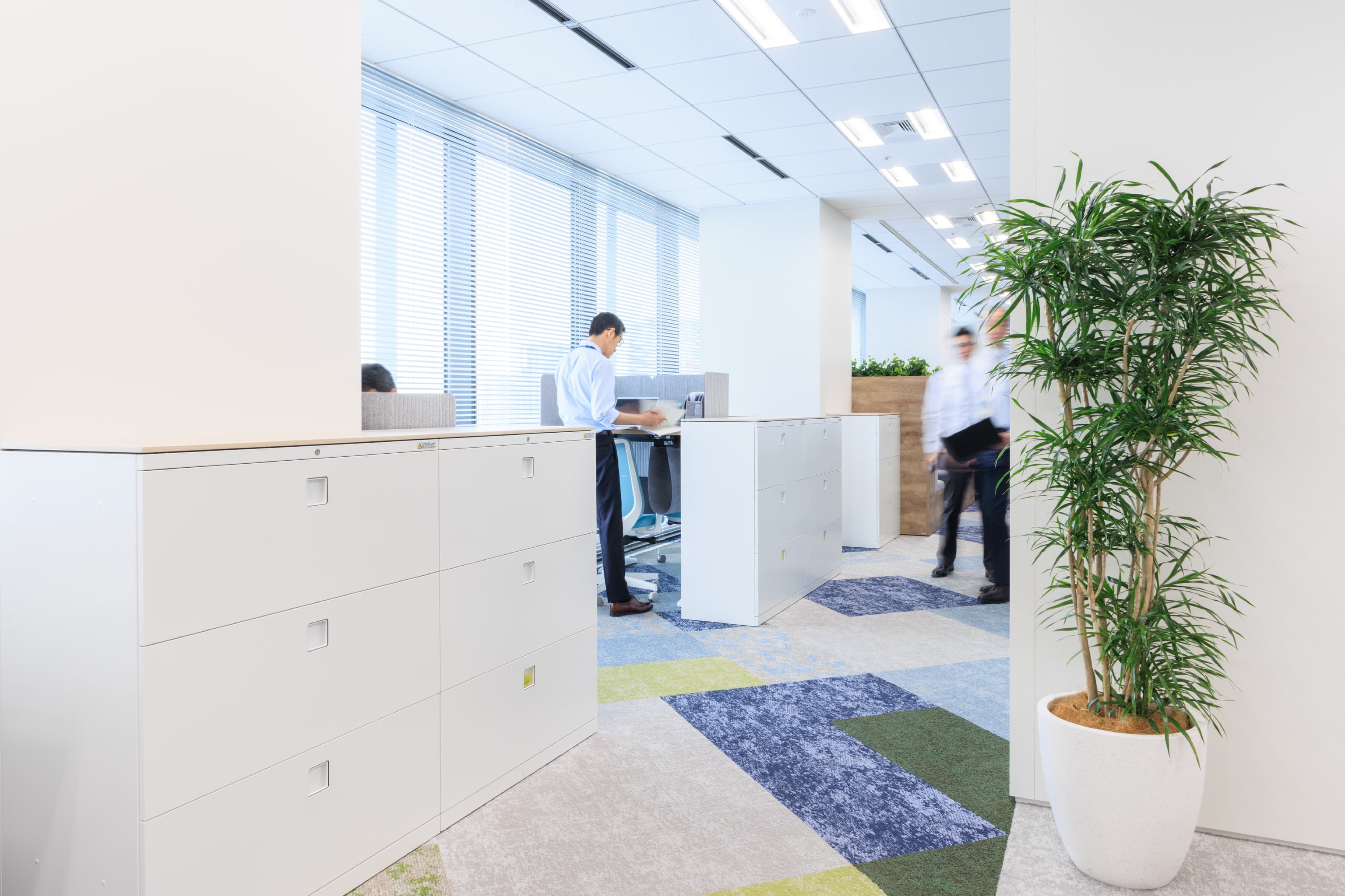 関西ペイント株式会社 様の事例写真／[執務エリア（ABWエリア）]ABWエリアで人気なのが、自由に高さを変えられる昇降デスク。健康のため、あるいは気分転換にと、利用する理由は人それぞれです。立って作業する従業員に通りかかった同僚が声をかけ、立ち話に発展することも。