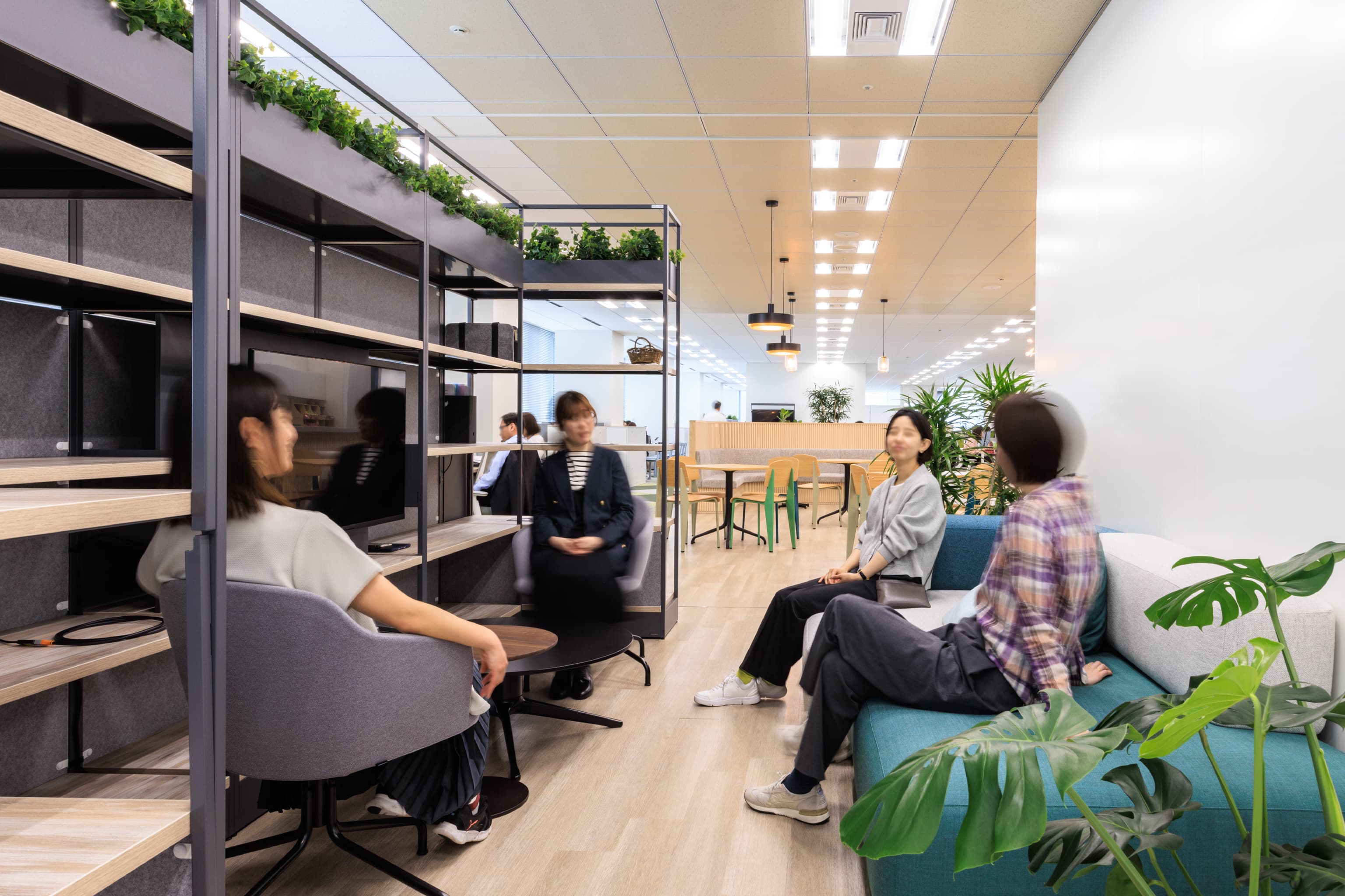 関西ペイント株式会社 様の事例写真／[カフェエリア]低めのソファやチェアが置かれた、ちょっとしたこもり空間。壁や棚に囲まれていて、周りの目を気にせずリラックスして過ごせます。従業員同士でのお悩み相談や気兼ねない雑談は仲間意識を育み、組織の絆を固くします。