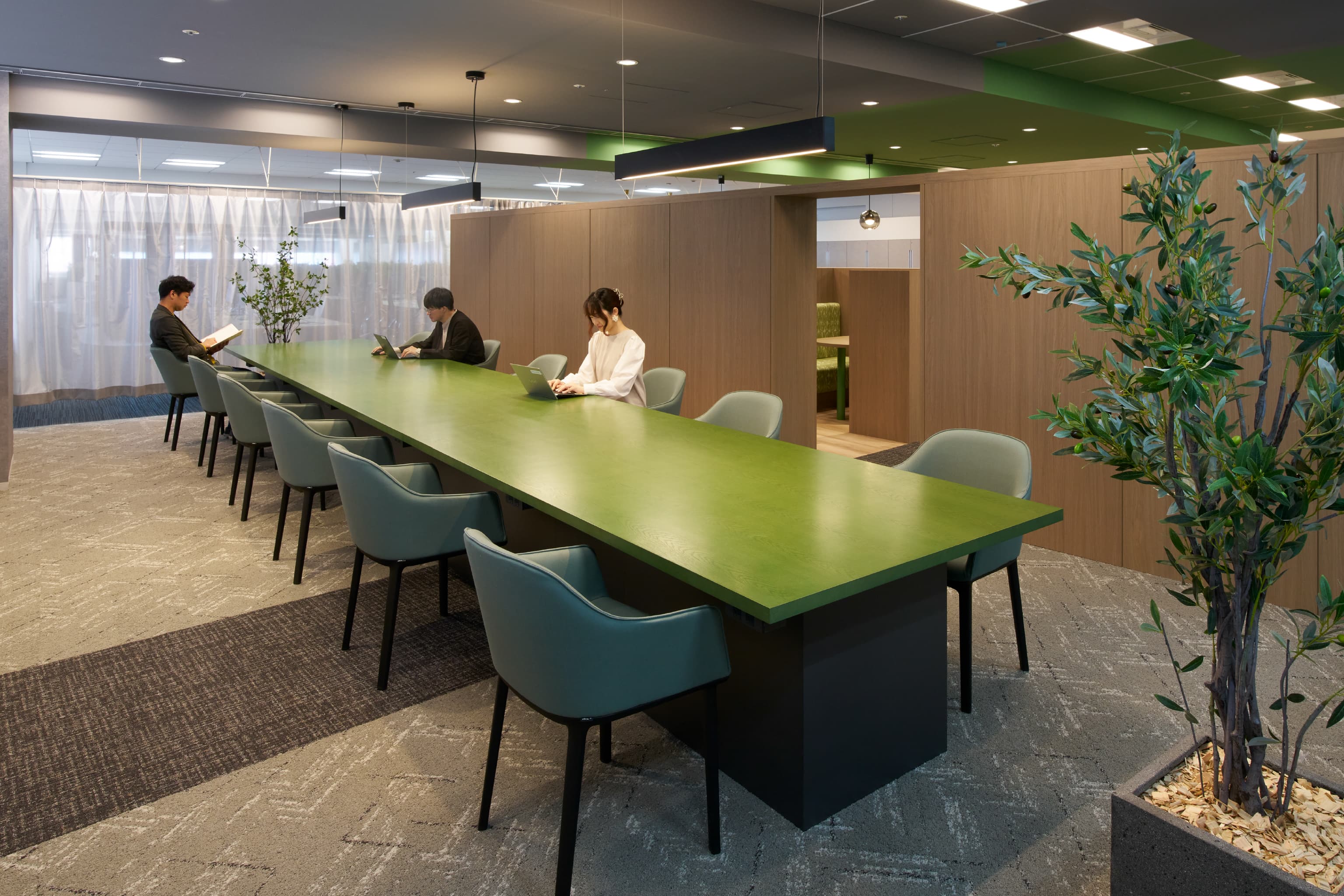 IQVIA ジャパン グループ 様の事例写真／[共創空間（6階STAGEエリア）]背の高い本棚の先には、図書館にいるかのような「こもり空間」が。長テーブルの天板もキーカラーで染色され、空間のまとまりを感じさせます。
