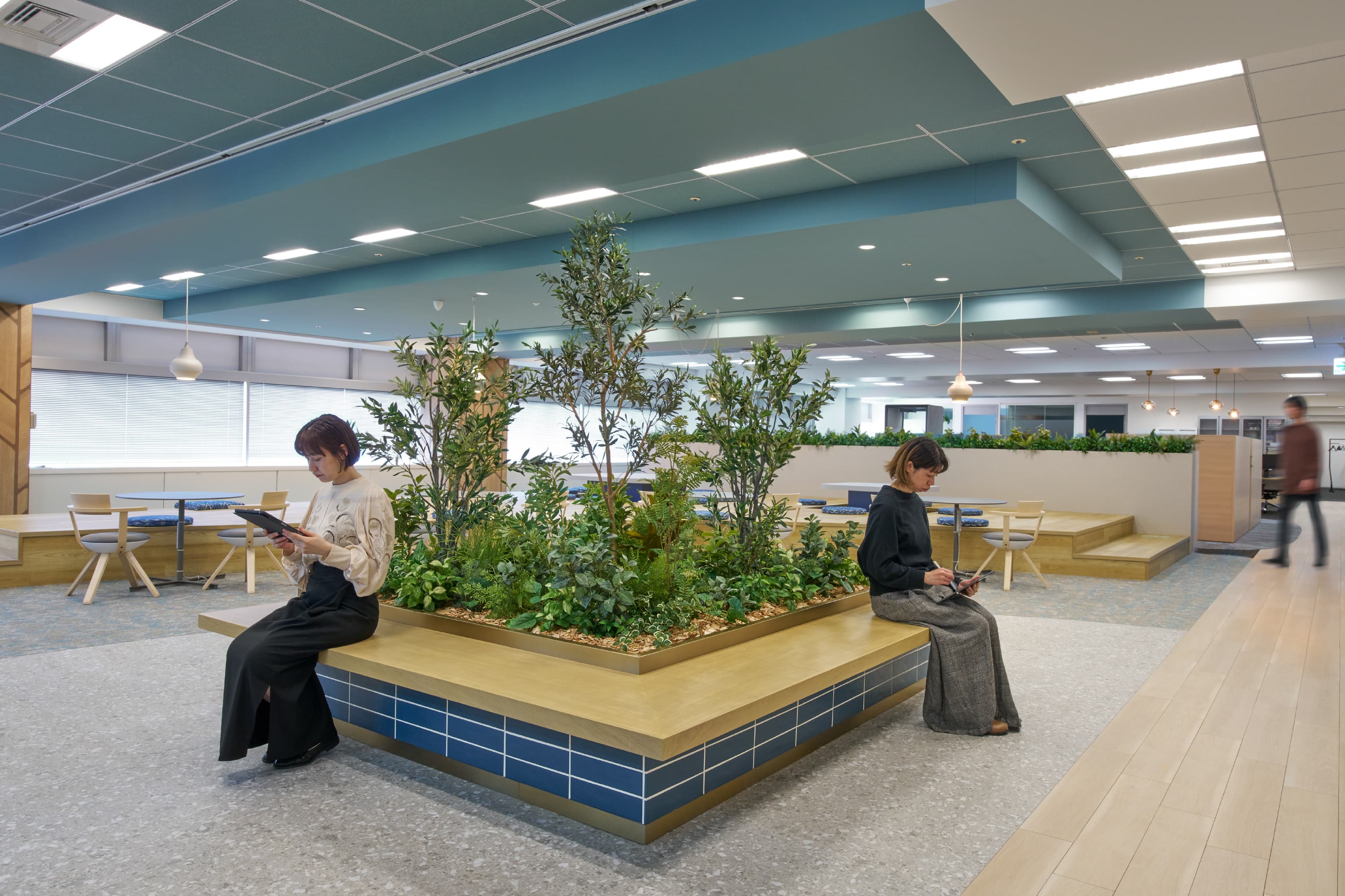 IQVIA ジャパン グループ 様の事例写真／[共創空間（7階STAGEエリア）]STAGEの中央には、目を引くシンボリックな植栽を配置。植栽をベンチと組み合わせることで、通路沿いを歩いてきた人が腰掛けて、くつろいだりおしゃべりしたりする場所になっています。