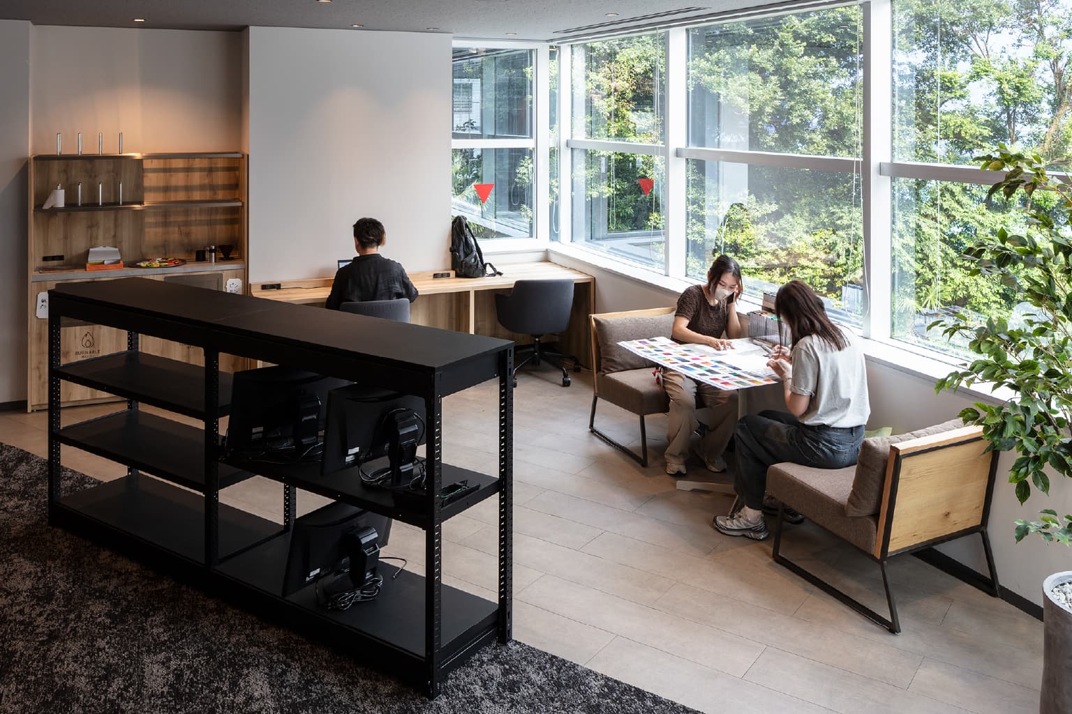 株式会社オカムラの事例写真／[カフェエリア]執務エリアの窓際に設けられたカフェエリアには、ソファなどカジュアルな家具が置かれています。窓の外に広がる緑を眺めながらリフレッシュ。社員同士の打ち合わせの場としても人気のスポットです。