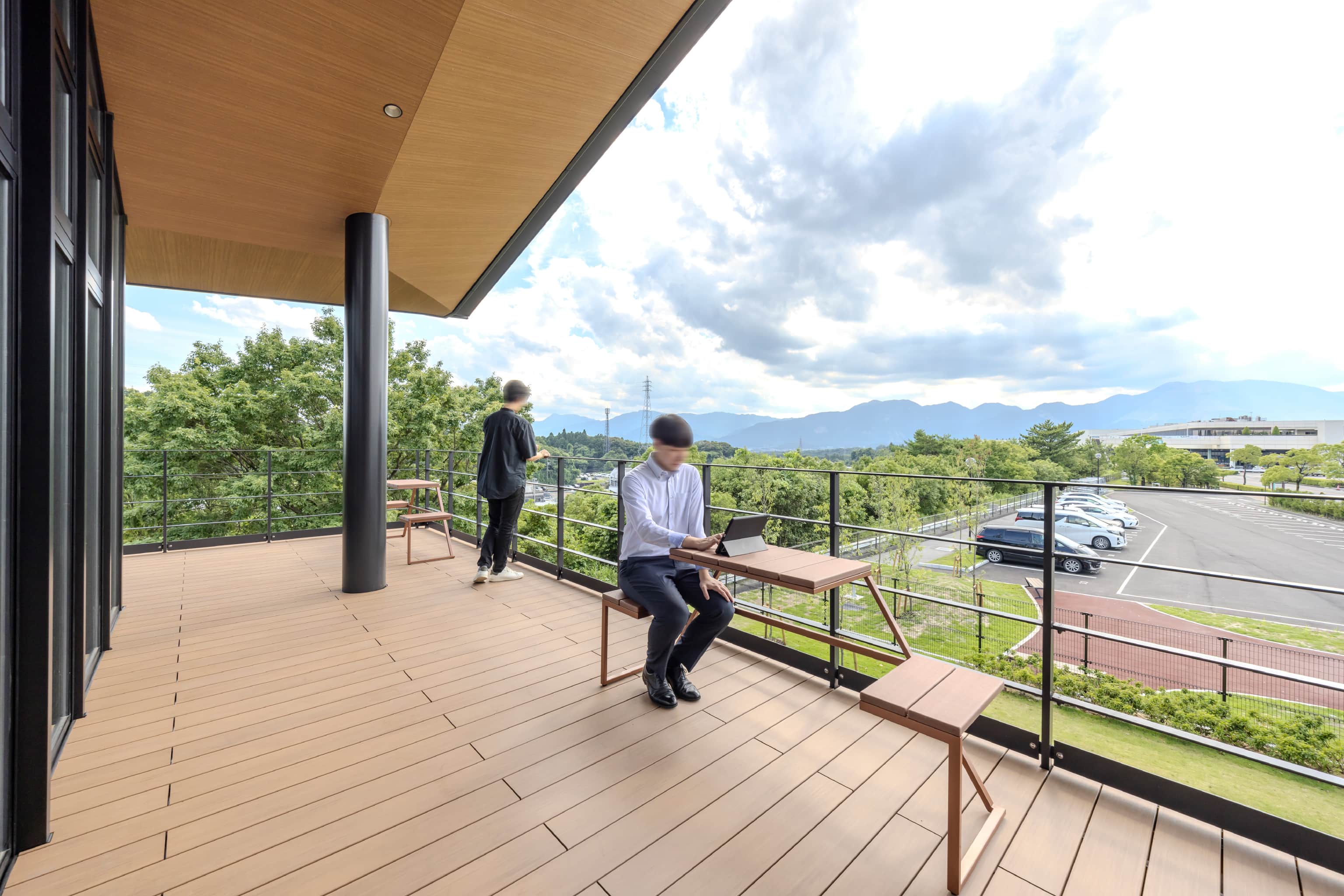 トヨタ車体株式会社 いなべ工場 様の事例写真／[2階展望デッキ]鈴鹿山脈の山々が一望できる2階の屋外スペース。軽い打合せや気分転換での活用、いなべの自然を満喫しながらランチを楽しむ従業員も。