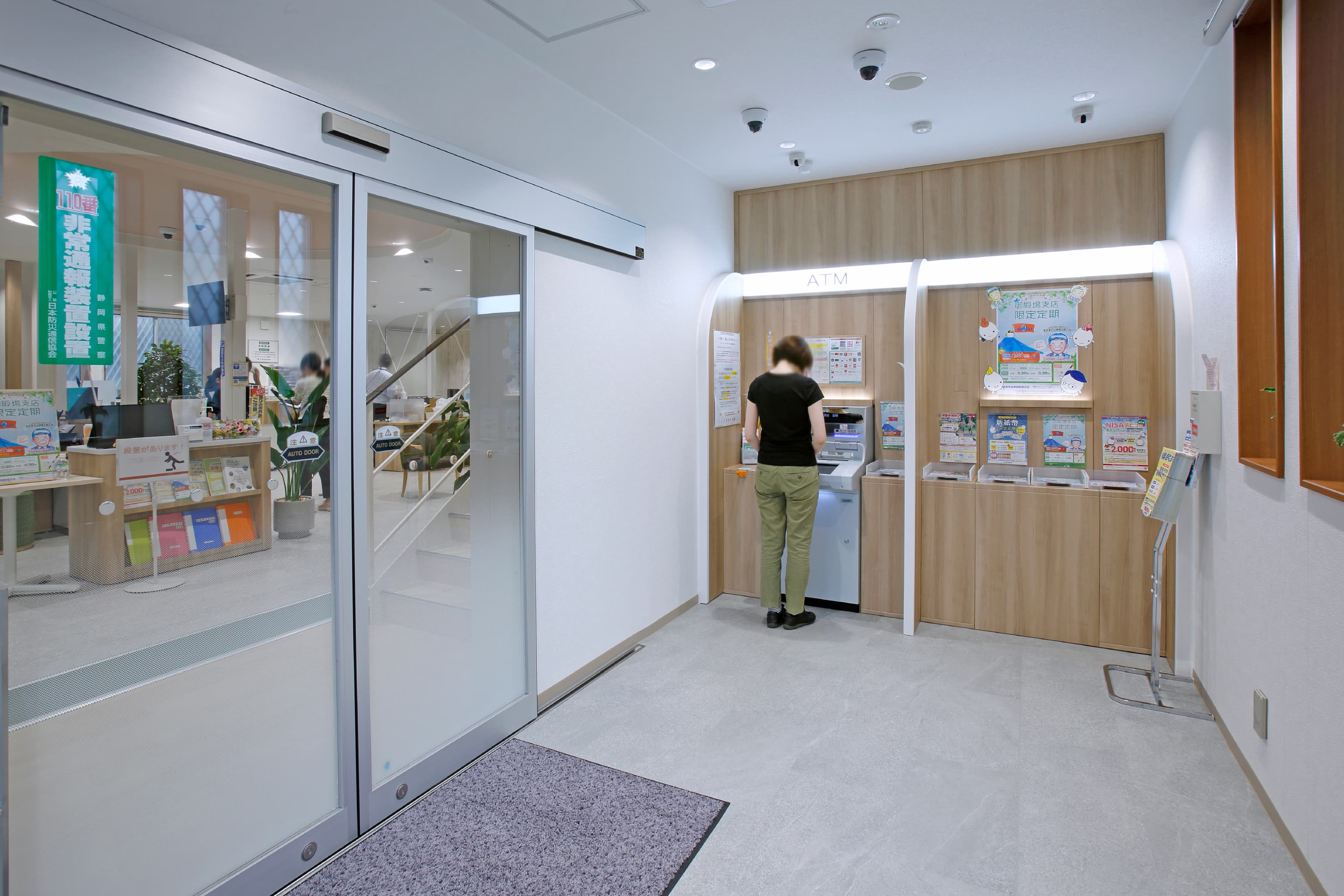 三島信用金庫 様の事例写真／[エントランス]ATMコーナーも木目のあしらいでナチュラルテイストに。来店客の増加に合わせ、2台目の設置も可能な造りです。開口部の広い入り口からは店内の様子が見え、活気を感じることができます。