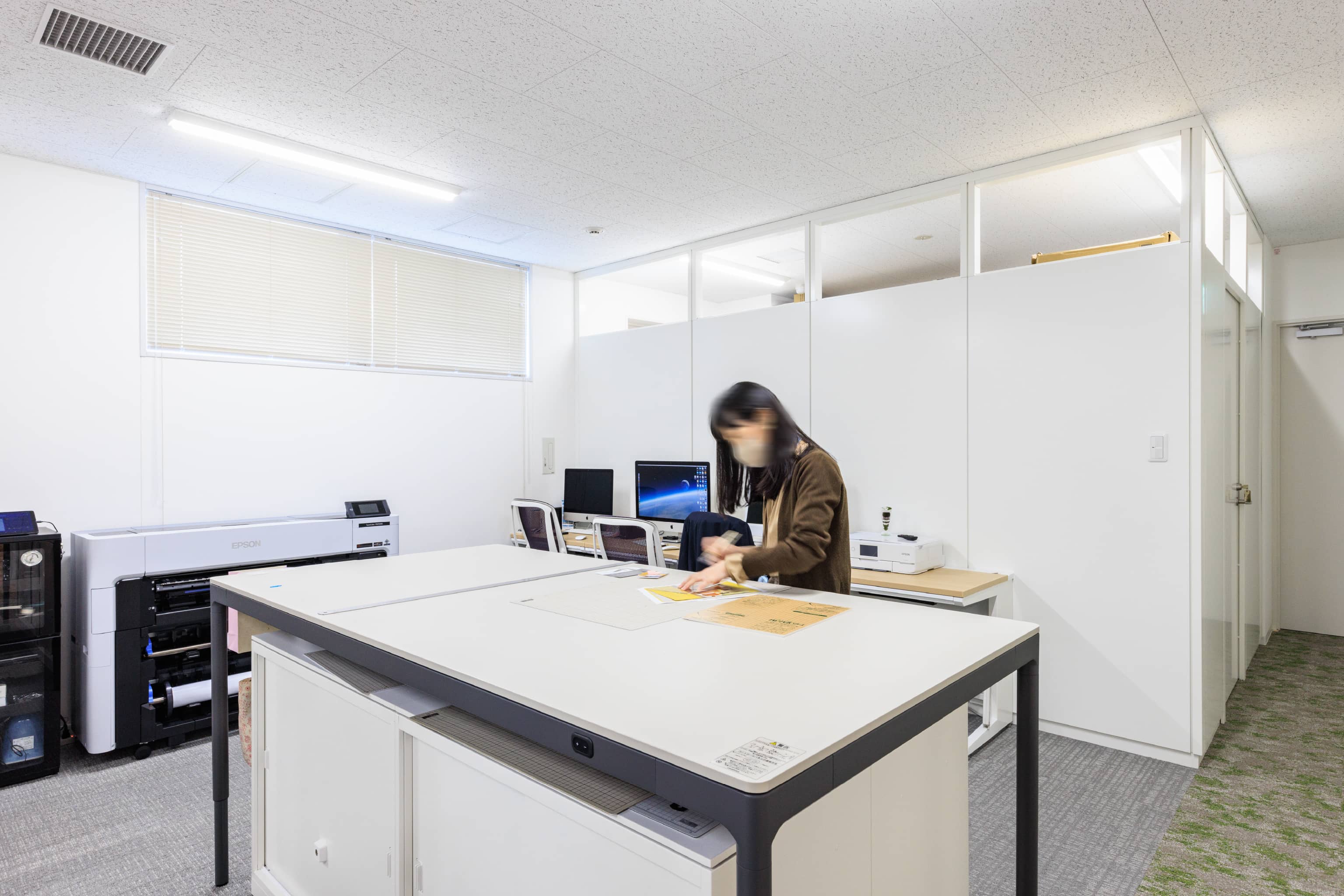 株式会社よーじや 様の事例写真／[作業スペース]店舗のディスプレイやポップの作成・印刷、商品準備などに使われる作業スペース。広いテーブル台は使う人の身長に合わせて上下昇降が可能です。天板には継ぎ目がなく、カッターを使える素材が使用されています。
