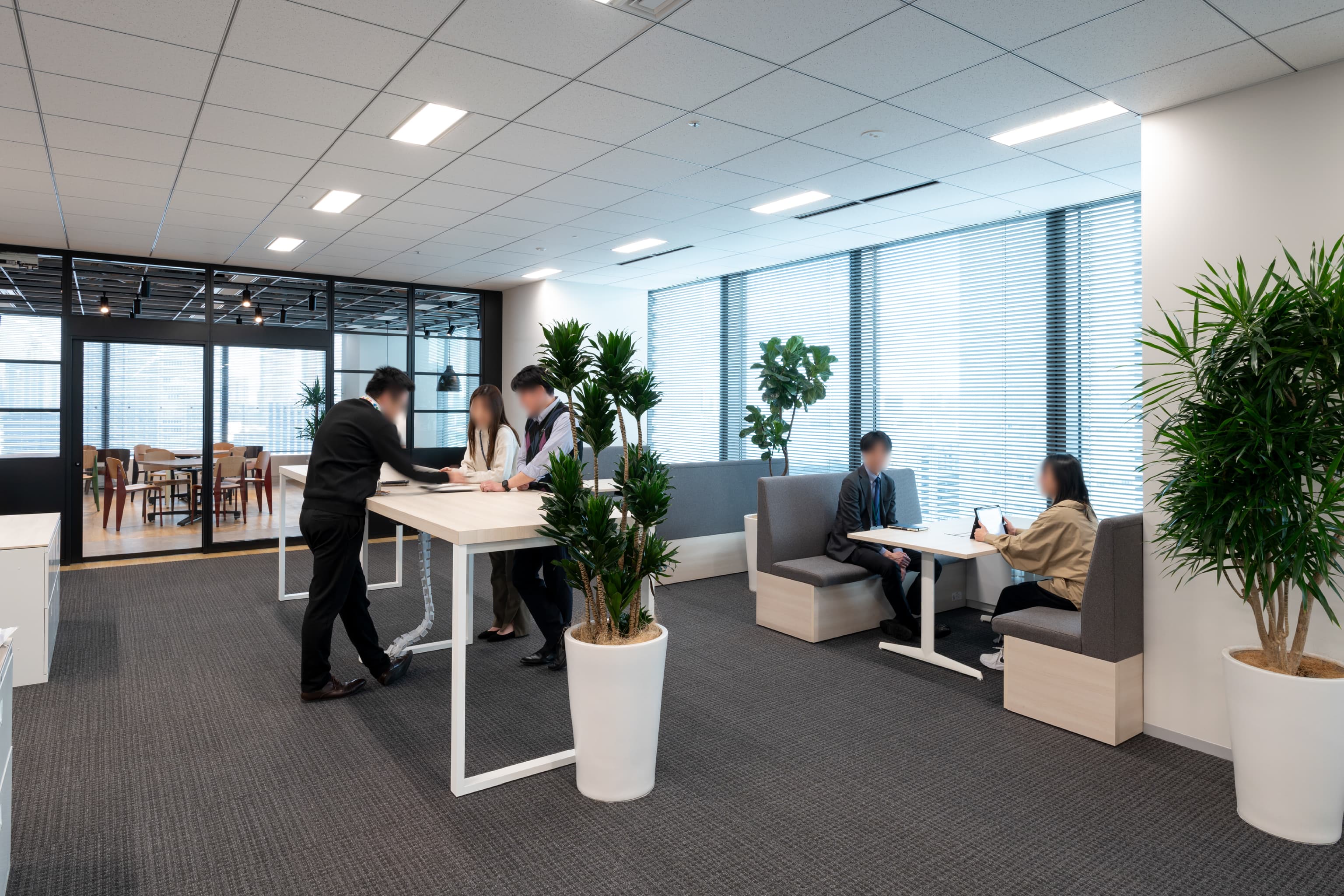 ハニューフーズ株式会社 様の事例写真／[執務エリア]窓際にはクイックな立ち会議に便利なハイタイプのデスクと、カジュアルな打ち合わせに適したファミレス席が配置されています。開放的で、気軽なコミュニケーションが生まれる場となっています。