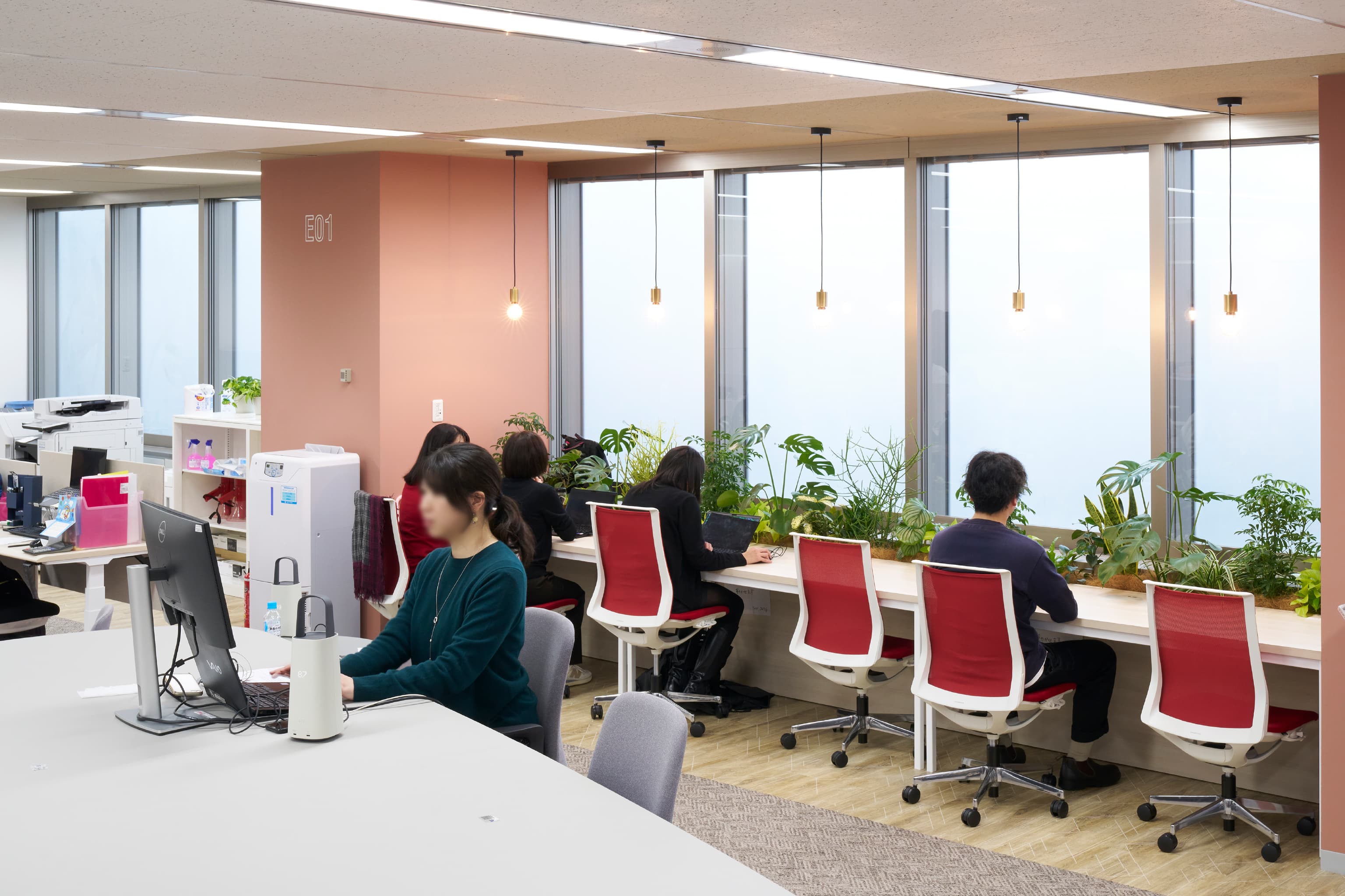 株式会社JALナビア 様の事例写真／[18F執務エリア（間接部門）]窓面にはコーポレートカラーの赤い椅子が置かれています。目の前の景色や植栽に癒されつつ、集中して仕事に取り組める人気の席です。