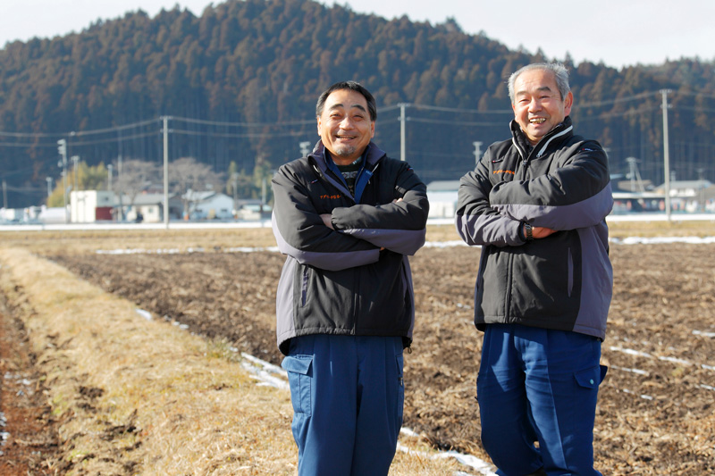 復旧させた農地をバックに微笑む安部社長（右）と佐々木常務（左）