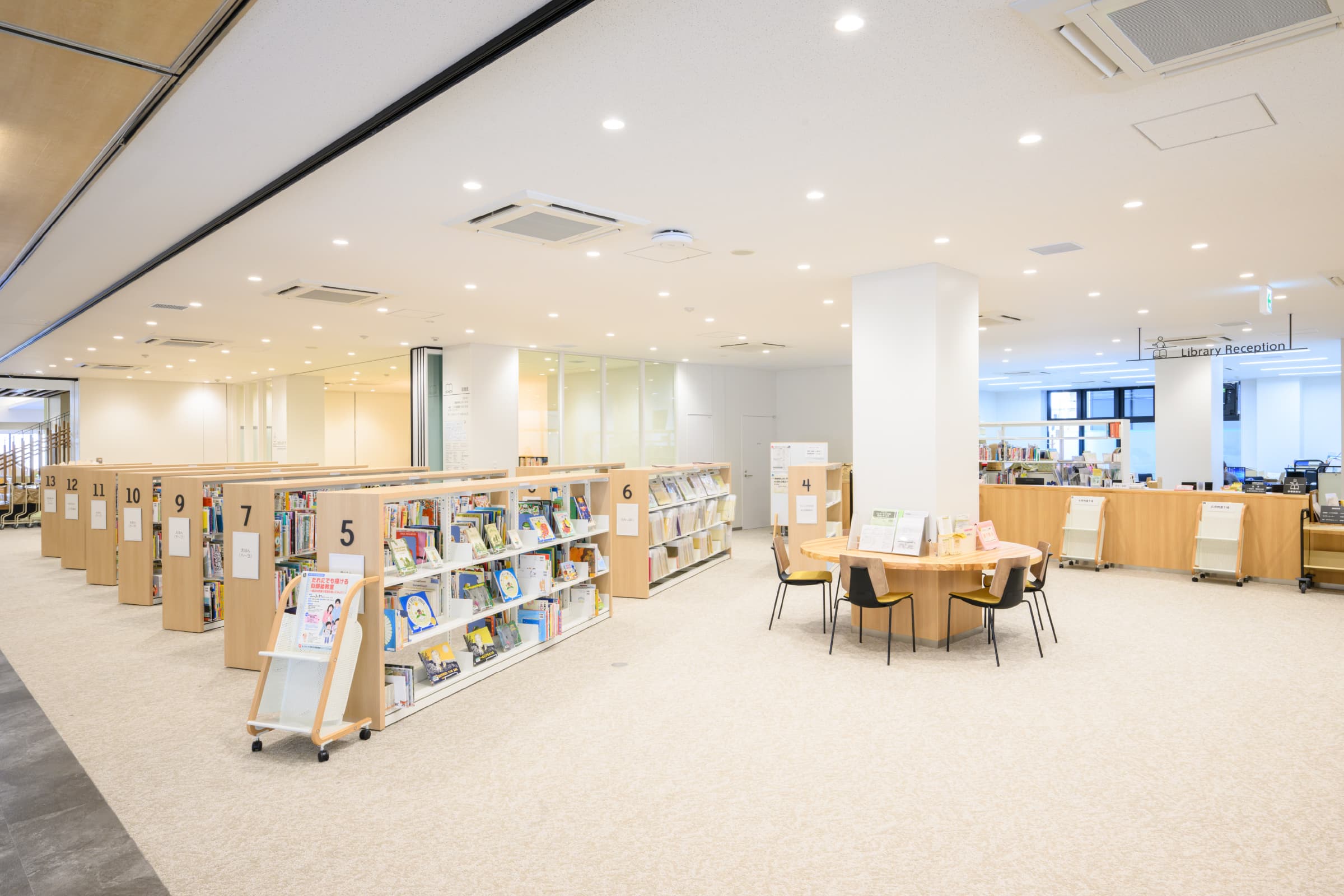 図書館受付／こども図書館スペースでは、本を手に取りやすいよう低書架を配置。受付からは周囲を見渡せ、利用者の困りごとにも対応しやすい。また受付前は広い空間で利用者も使いやすい。