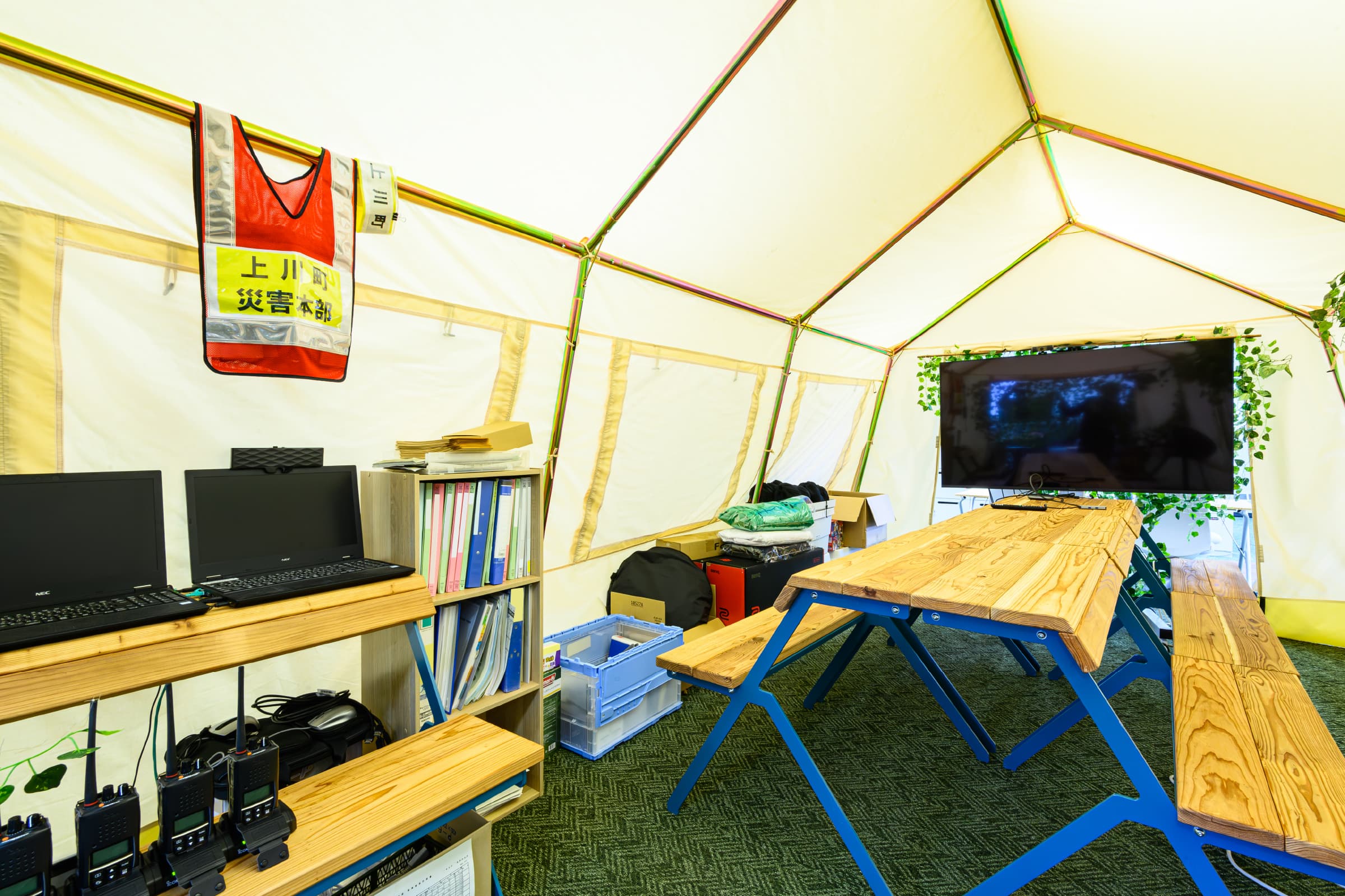 テントスペース／木材利用のキャンプ什器やグリーンを採用し、明るく温かみのある空間へ。適度なこもり感があり、会議やミーティングスペースとして活用しており、災害時には、災害対策本部としての運用を想定。